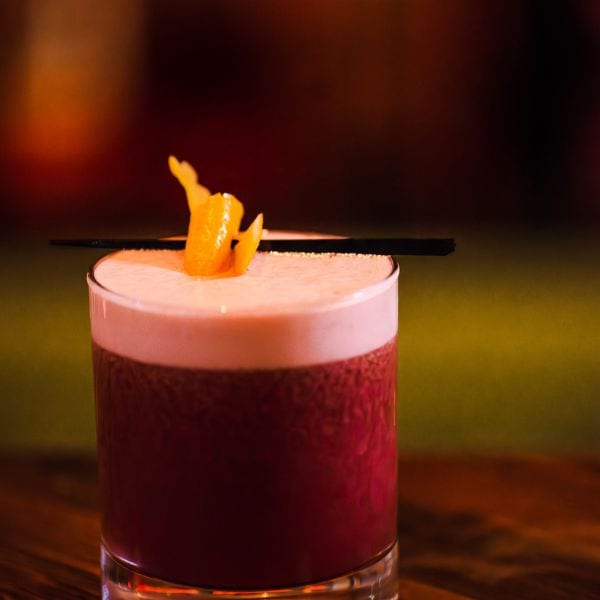 A blackberry whiskey sour with an orange twist